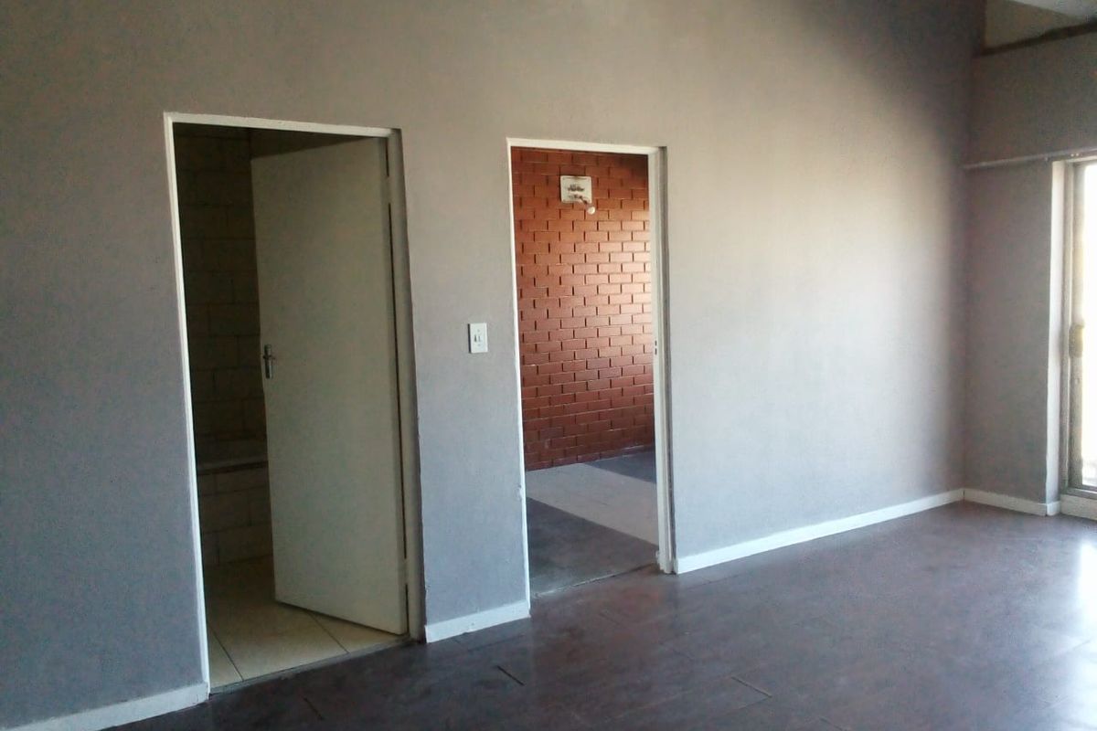 An empty living area featuring dark tiled flooring, neutral grey walls, and access to adjacent rooms with exposed brick detailing.