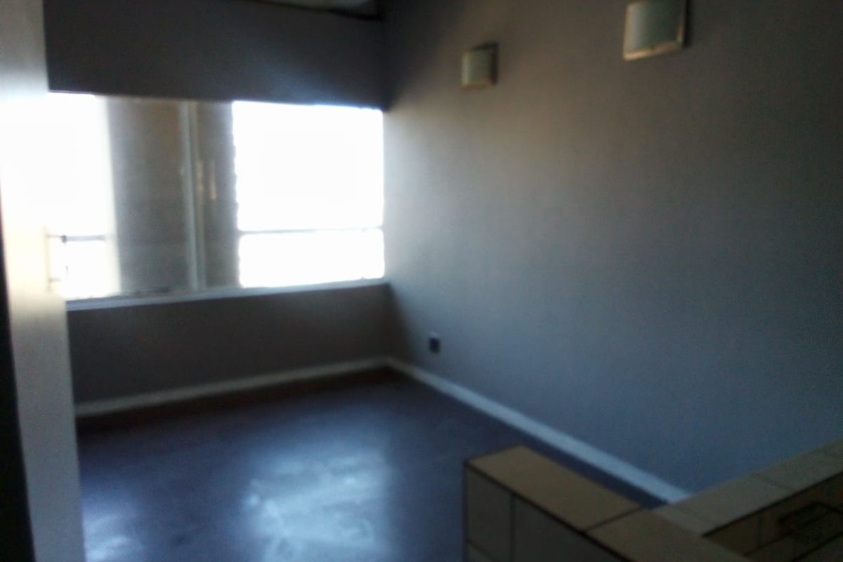 An empty bedroom featuring grey walls, wall-mounted lighting, and a large window providing natural light.