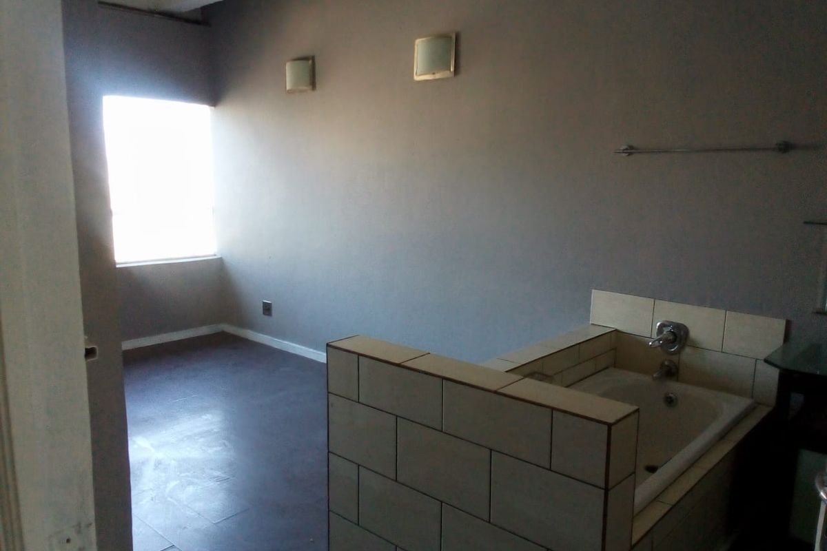 An empty bathroom featuring a built-in bathtub with tiled surround and wall-mounted lighting, requiring cosmetic updates to improve the overall finish.