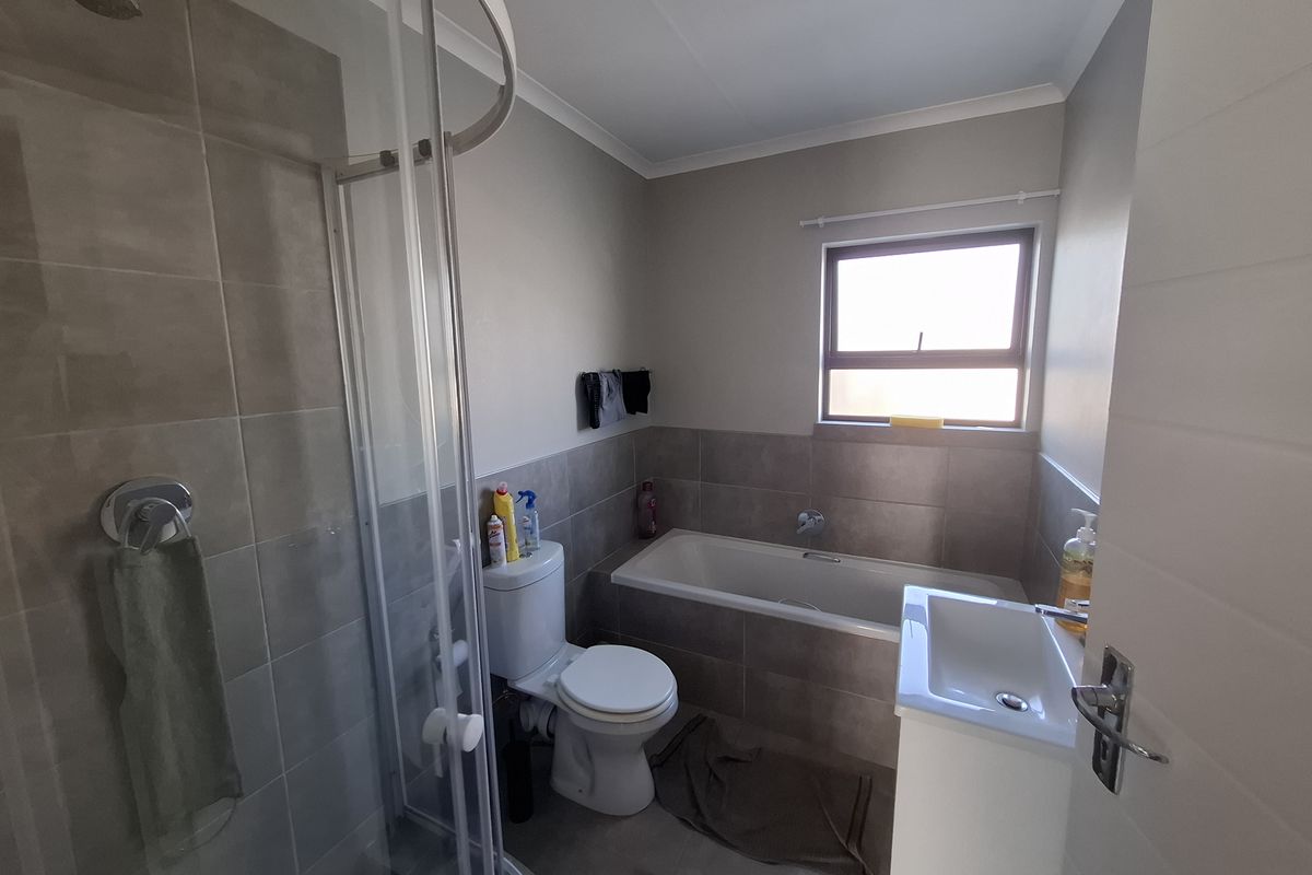 A functional bathroom featuring a glass shower enclosure, a bathtub, a toilet, and a vanity basin with neutral wall and floor tiling.