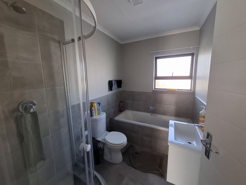 A functional bathroom featuring a glass shower enclosure, a bathtub, a toilet, and a vanity basin with neutral wall and floor tiling.