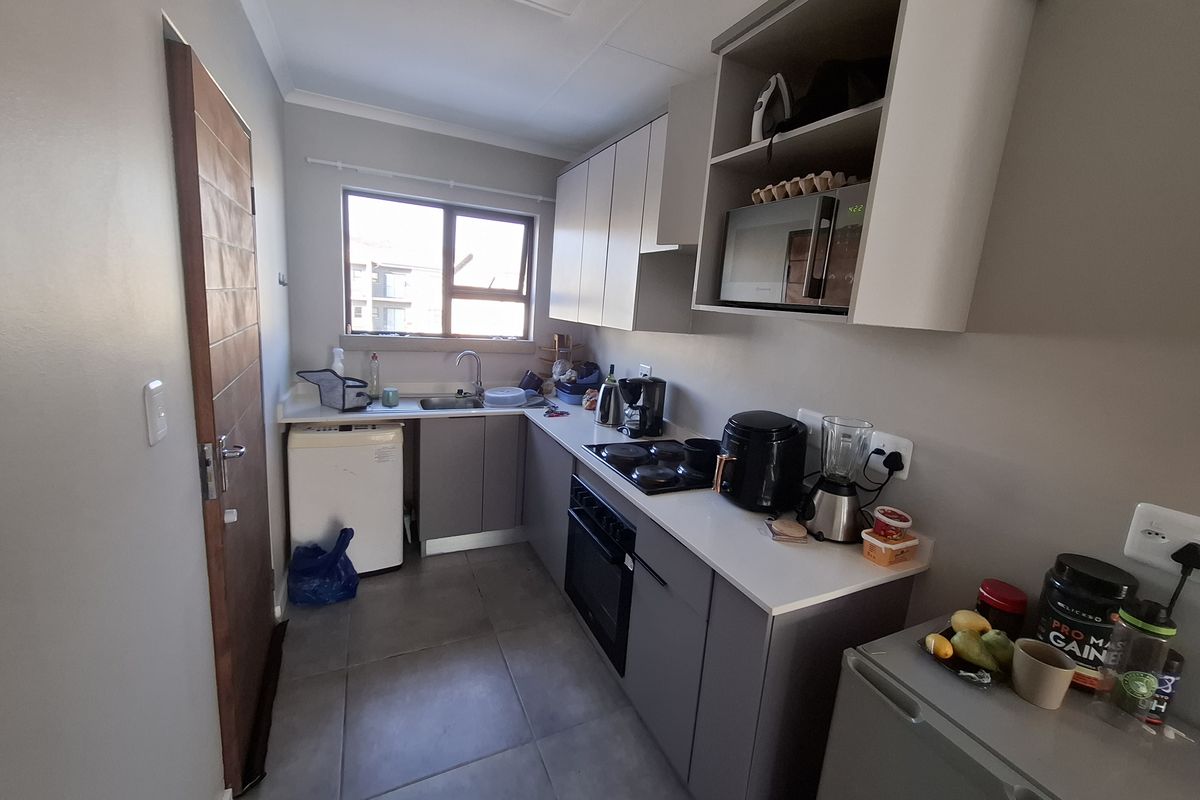 A functional kitchen featuring modern grey cabinetry, laminate countertops, a built-in oven with electric hob, and tiled flooring.