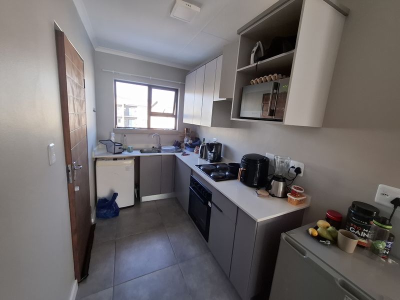 A functional kitchen featuring modern grey cabinetry, laminate countertops, a built-in oven with electric hob, and tiled flooring.