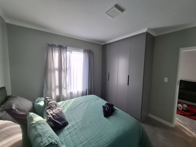 A well-maintained bedroom featuring neutral grey walls, a large built-in wardrobe, and natural light through the window.