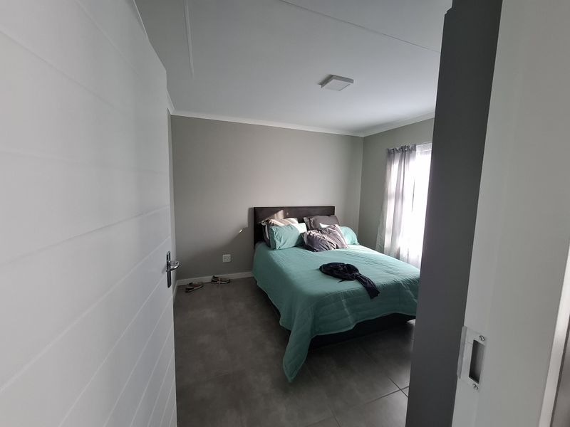 A well-lit bedroom featuring neutral wall tones, modern tiled flooring, and a sliding door entrance.