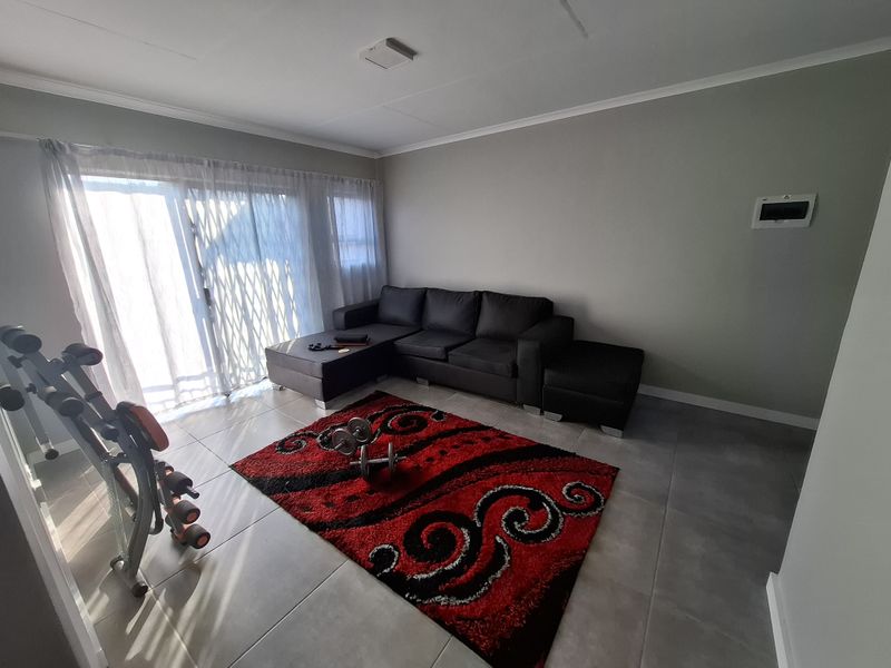 A bright living room featuring large sliding glass doors with security gates and neutral tiled flooring.