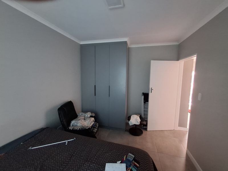 A bedroom featuring neutral grey walls, tiled flooring, and modern built-in cupboards with matte grey doors.