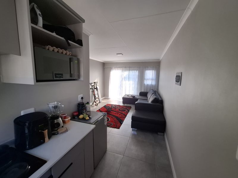 Open-plan living area featuring a compact kitchen with built-in cabinetry and microwave, leading to a bright lounge space with sliding door access.