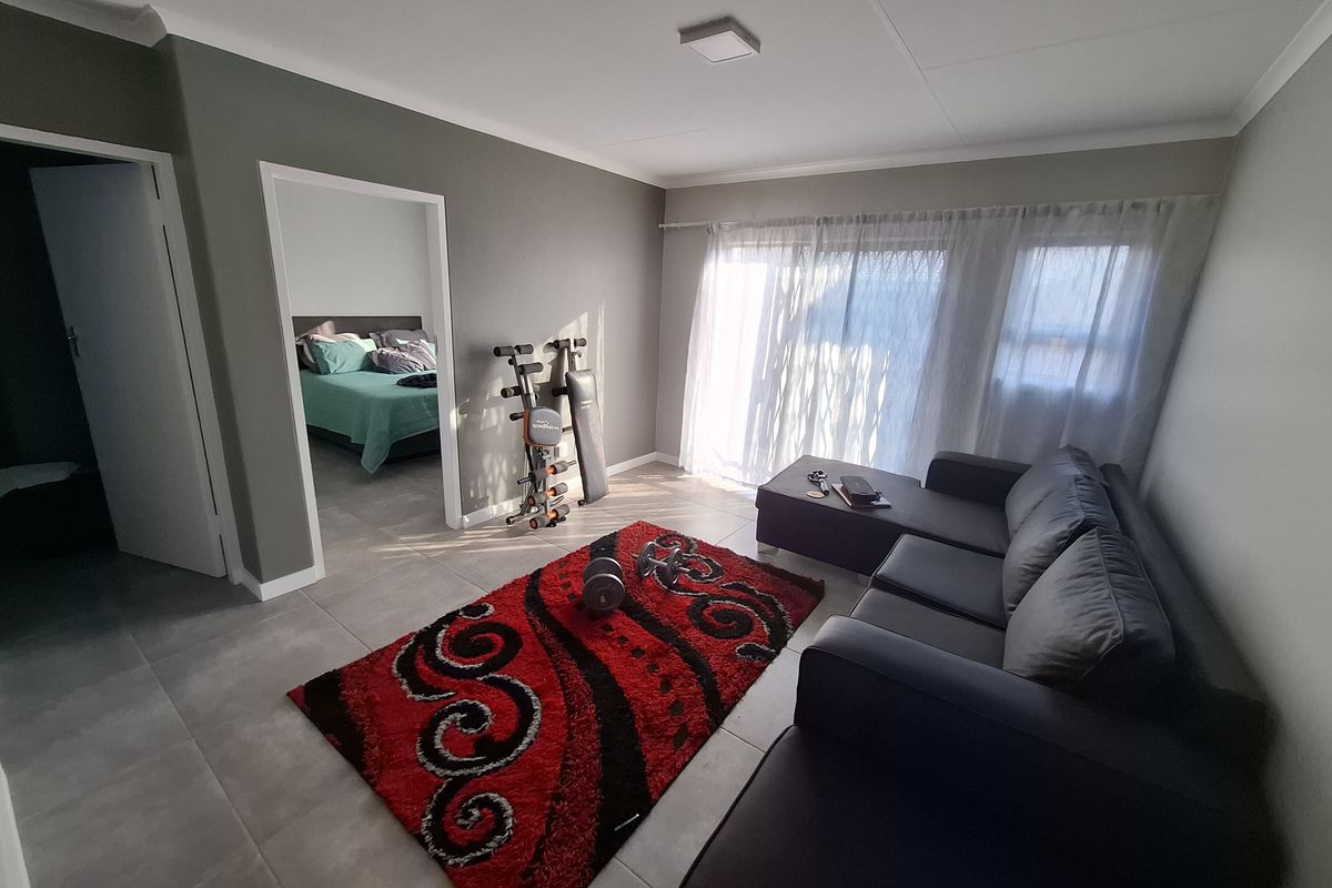 A well-lit living room featuring neutral grey walls, large format floor tiles, and a sliding glass door providing access to the exterior.