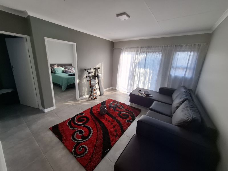 A well-lit living room featuring neutral grey walls, large format floor tiles, and a sliding glass door providing access to the exterior.