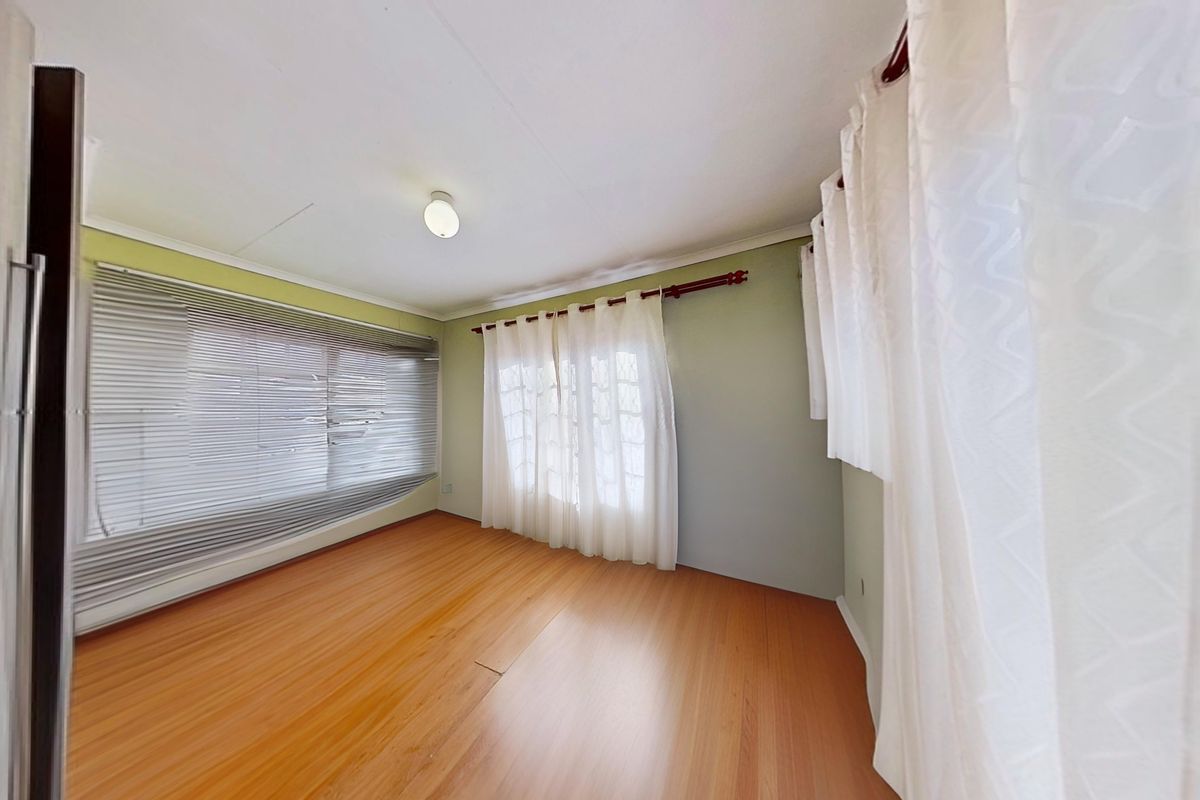 A bright, empty bedroom featuring wood-look laminate flooring, large windows with blinds, and neutral wall finishes.