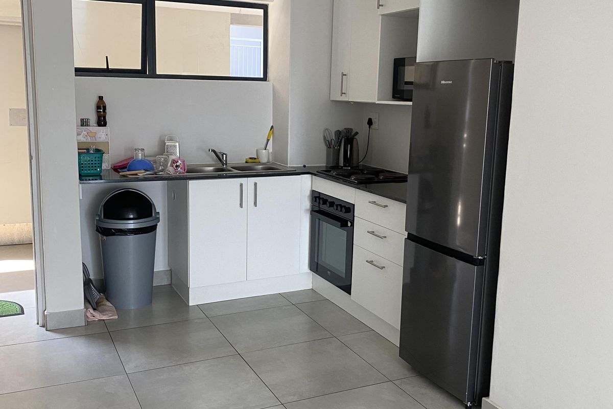 A compact, modern kitchen featuring white cabinetry, tiled flooring, a built-in oven, hob, and stainless steel sink.