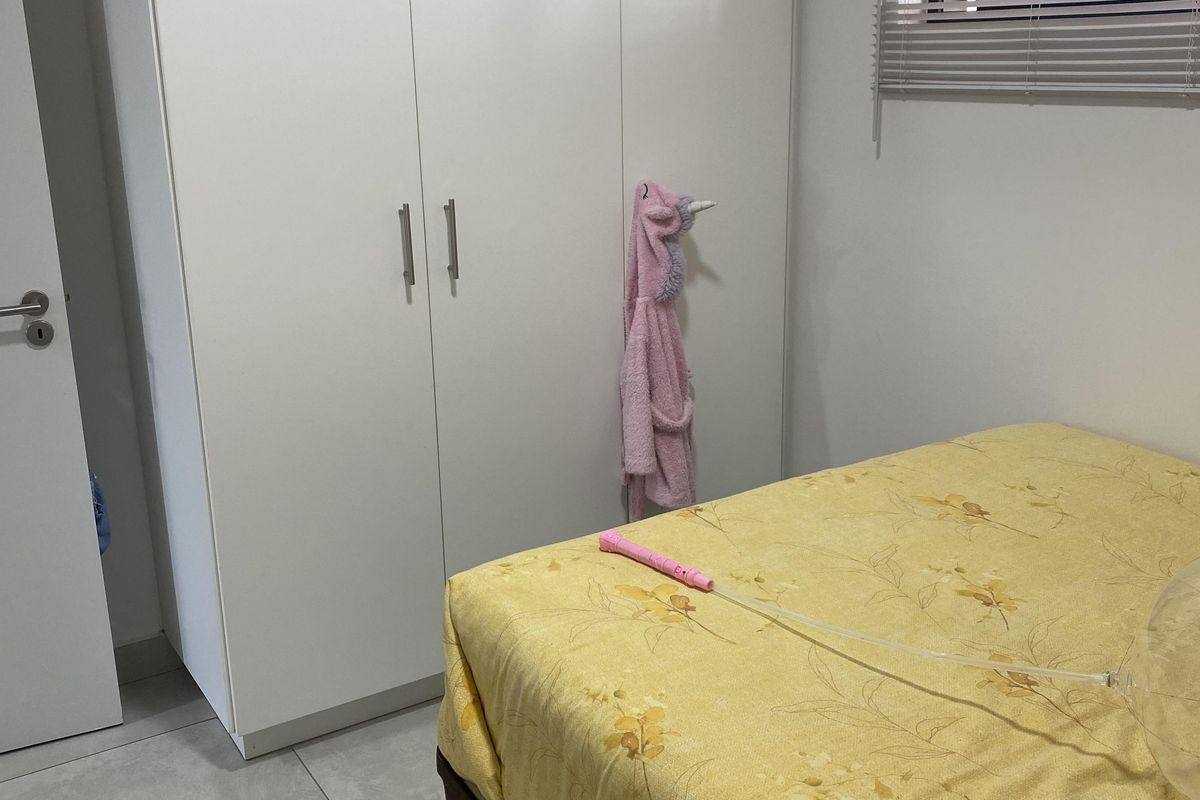 A bedroom featuring built-in white cabinetry, tiled flooring, and a window fitted with horizontal blinds.