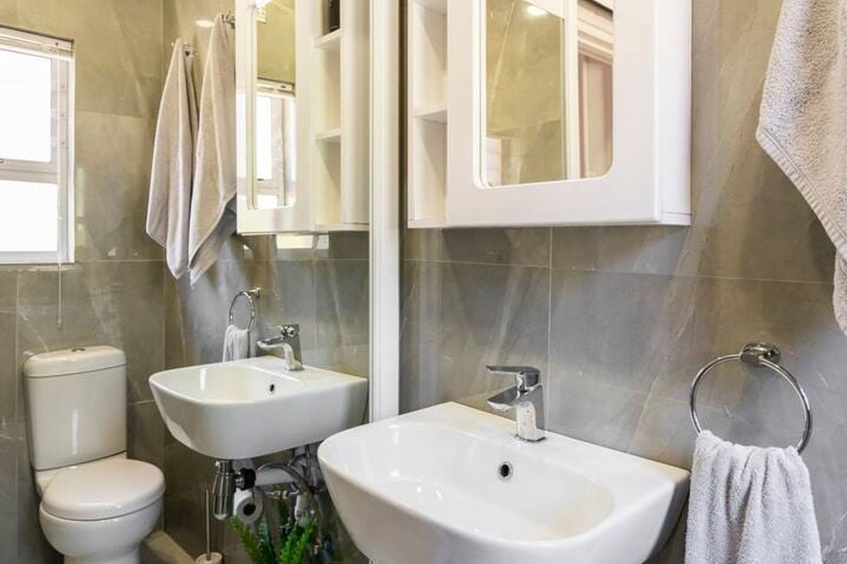 A modern bathroom featuring grey wall tiles, a wall-mounted basin, a toilet, and a large mirror with an integrated medicine cabinet.