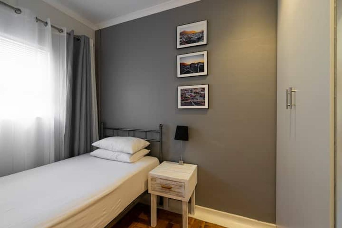A compact bedroom featuring parquet flooring, a built-in wardrobe, and a neutral grey accent wall, offering a clean and functional living space.