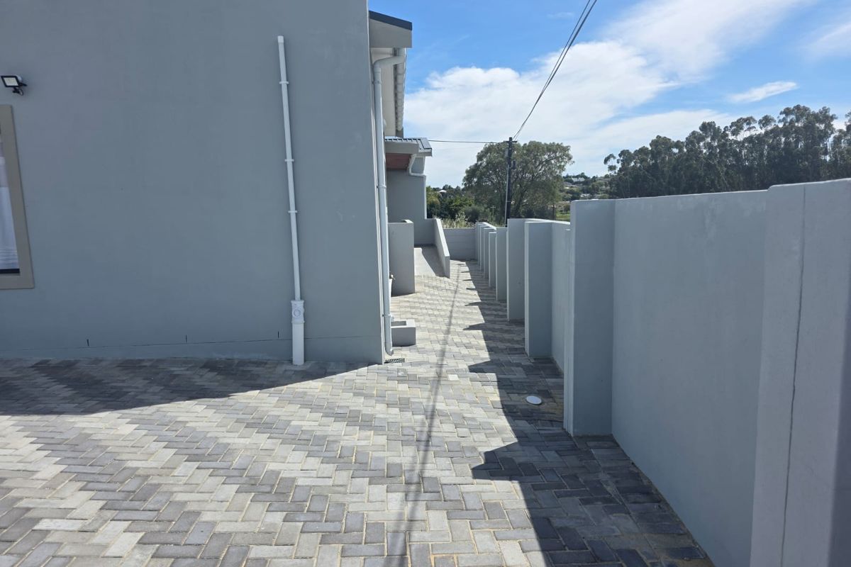A side exterior view of the property featuring paved walkways and a modern boundary wall.