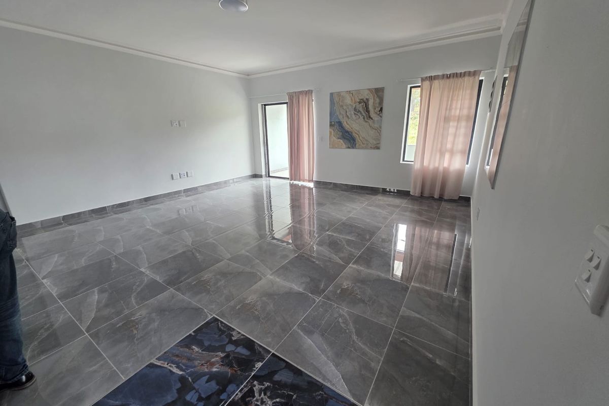 A spacious, empty living area featuring modern large-format grey tiled flooring and direct access to an outdoor space through a sliding glass door.