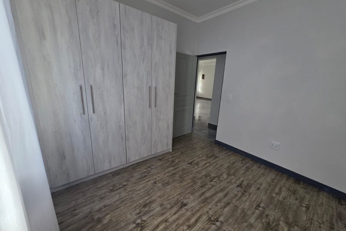 A clean bedroom featuring wood-look laminate flooring and modern built-in cupboards with a light wood finish.