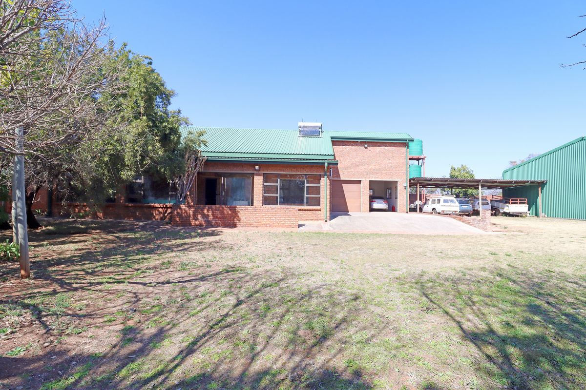 A farm-style residence featuring a green corrugated metal roof, brick facade, integrated garage, and an adjacent covered carport area on a spacious plot.