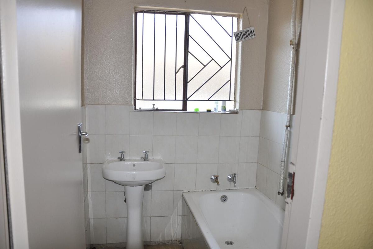 A functional bathroom featuring a pedestal basin, bathtub, and security bars on the window. The space requires cosmetic updates to modernize the finishes.