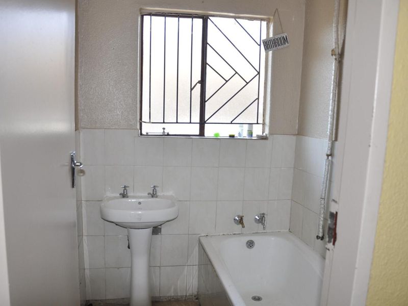A functional bathroom featuring a pedestal basin, bathtub, and security bars on the window. The space requires cosmetic updates to modernize the finishes.