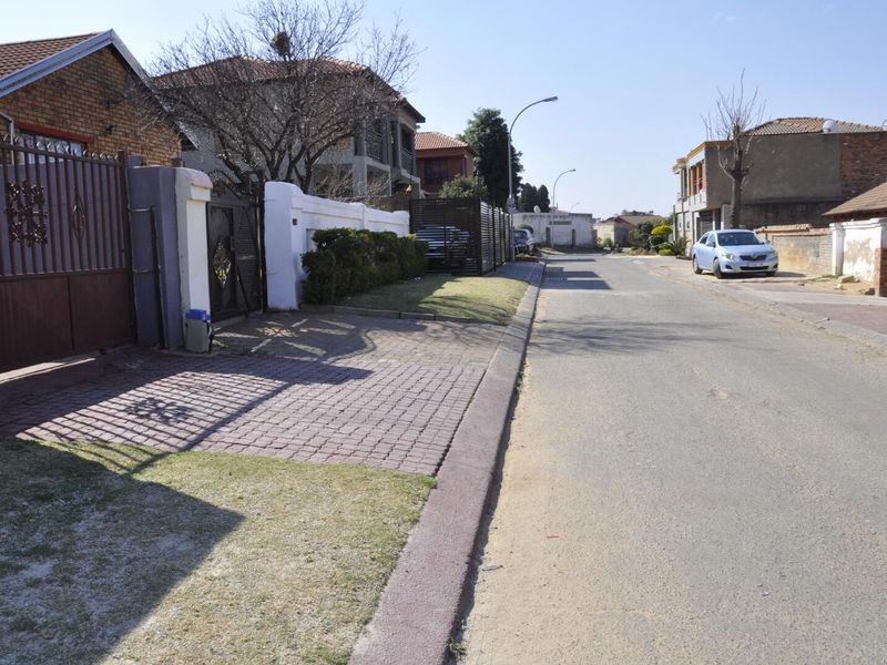 A street view showing the residential road, paved driveway entrance, and perimeter boundary wall of the property.