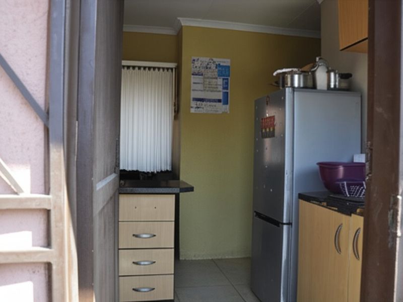 A compact kitchen area featuring built-in cabinetry, laminate countertops, and tiled flooring, viewed from the entrance.