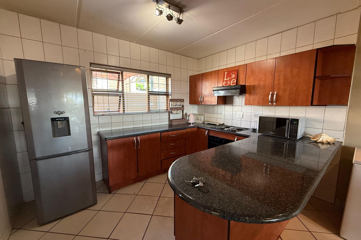 Functional kitchen featuring granite countertops, wooden cabinetry, a breakfast nook, and a tiled backsplash, offering a practical layout for daily meal preparation.