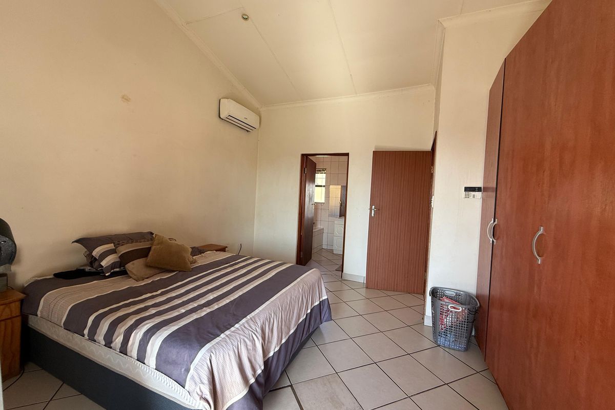 Spacious bedroom featuring tiled flooring, built-in cupboards, and a wall-mounted air conditioning unit, with direct access to an en-suite bathroom.