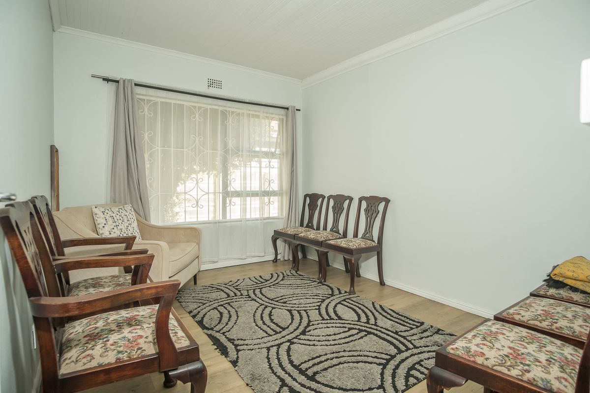 A living room featuring light-toned flooring, a large window with security bars, and crown molding.