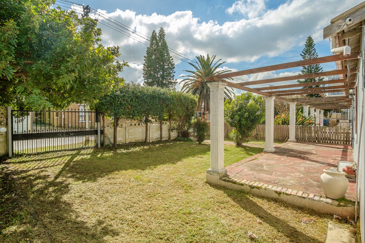 Rear garden featuring a paved patio area with a timber pergola, established trees, and a metal security gate.