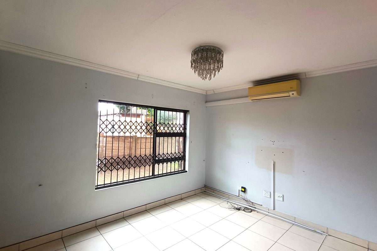 An empty living room featuring tiled flooring, a security gate on the window, and an installed air conditioning unit.