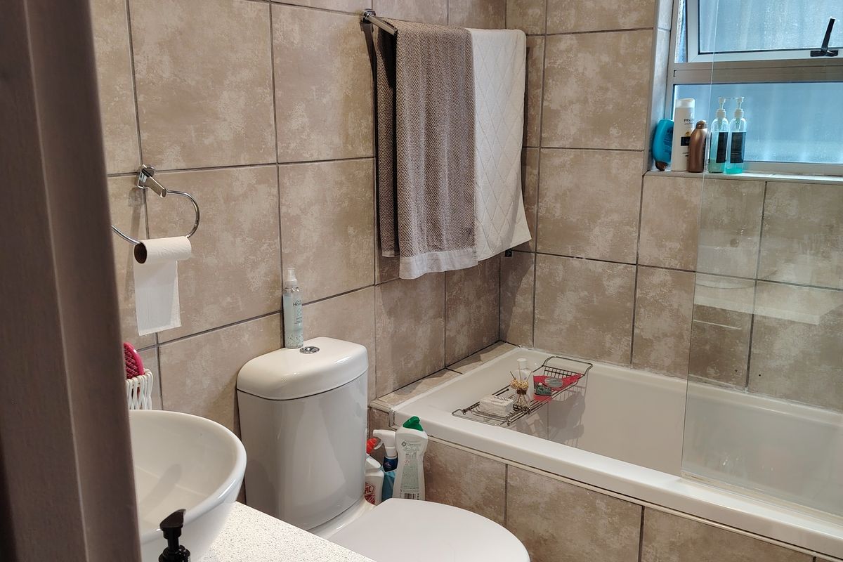 A functional bathroom featuring a bathtub with a glass screen, a vanity basin, and neutral wall and floor tiling.