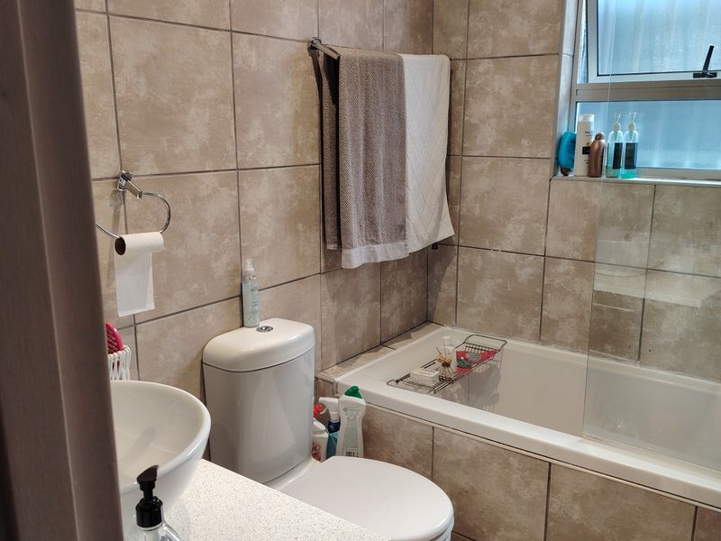 A functional bathroom featuring a bathtub with a glass screen, a vanity basin, and neutral wall and floor tiling.