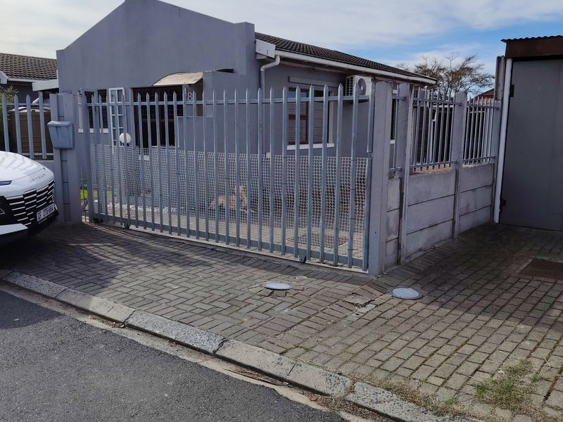 Front exterior view of a residential house featuring a paved driveway, metal security fencing, and a sliding gate.