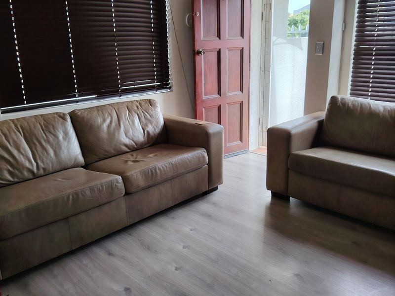 A living room featuring laminate flooring, timber door access to the exterior, and a wall-mounted air conditioning unit.