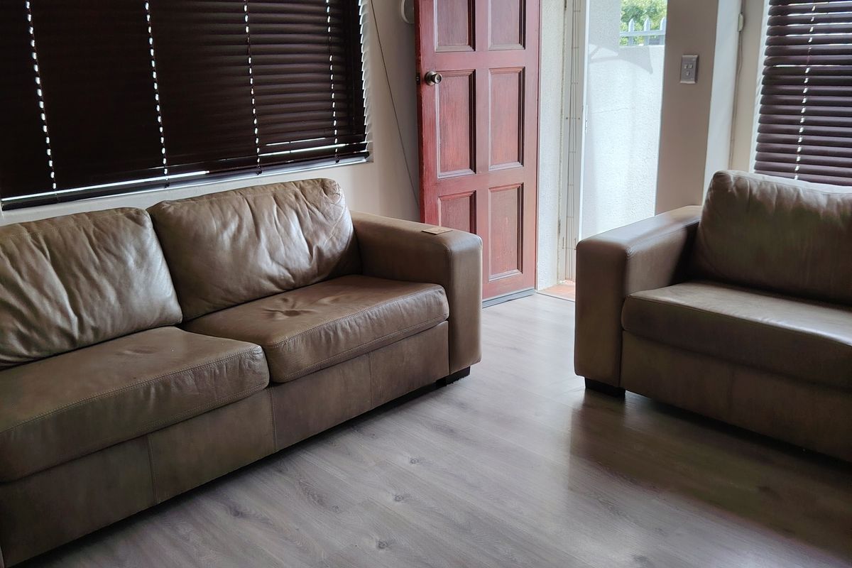 A living room featuring laminate flooring, timber door access to the exterior, and a wall-mounted air conditioning unit.