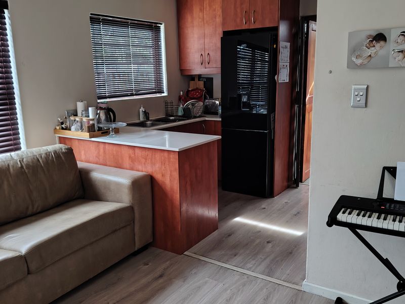 Open-plan living area featuring laminate flooring and a compact kitchen with built-in cabinetry and a breakfast counter.