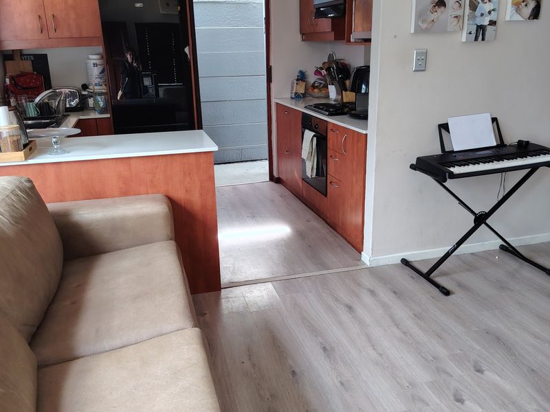 Open-plan kitchen and living area featuring wood-finish cabinetry, integrated appliances, and light-toned laminate flooring with direct access to an exterior utility area.