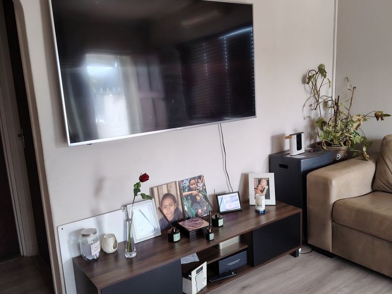 A living room area featuring laminate flooring, a wall-mounted television, and a classic archway leading to an adjacent space.