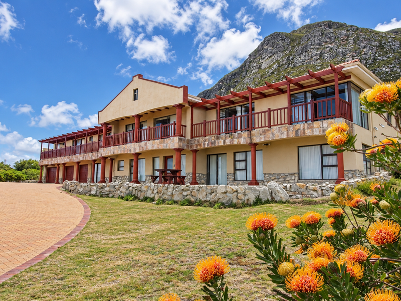 Spacious multi-level residence featuring stone cladding, timber pergolas, and a paved driveway, set against a scenic mountain backdrop.