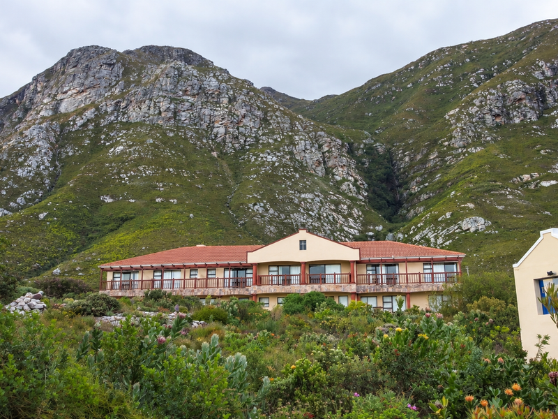 A scenic rear view of a multi-level residence featuring a terracotta roof, timber balcony, and stone accents, set against a dramatic mountain backdrop.