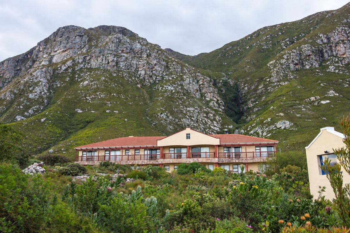 A scenic rear view of a multi-level residence featuring a terracotta roof, timber balcony, and stone accents, set against a dramatic mountain backdrop.