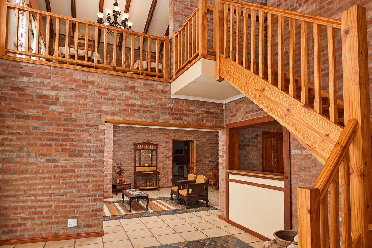 Spacious living area featuring exposed brick walls, a prominent timber staircase, and a mezzanine level with vaulted ceilings and exposed timber beams.