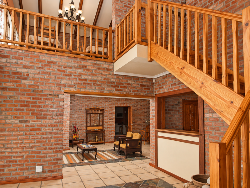 Spacious living area featuring exposed brick walls, a prominent timber staircase, and a mezzanine level with vaulted ceilings and exposed timber beams.