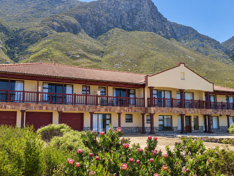 A spacious two-story residence featuring stone cladding, a large upper-level balcony with timber railings, and multiple garage doors, set against a scenic mountain backdrop.