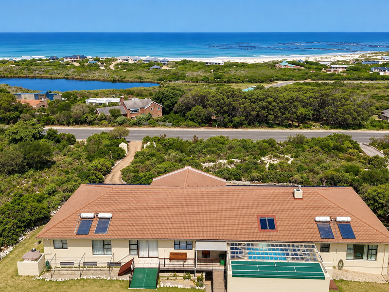 Aerial view of the property featuring a tiled roof with solar panels, a covered swimming pool, and a deck, set against a coastal landscape.
