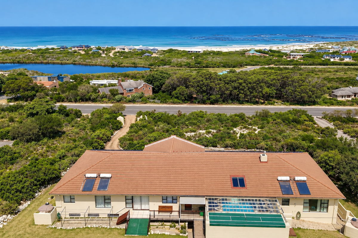 Aerial view of the property featuring a tiled roof with solar panels, a covered swimming pool, and a deck, set against a coastal landscape.
