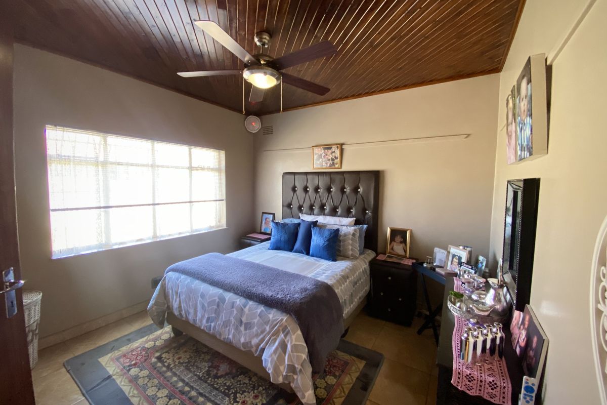 A bedroom featuring a distinctive timber tongue and groove ceiling, ceiling fan, and tiled flooring, offering a cozy and functional living space.