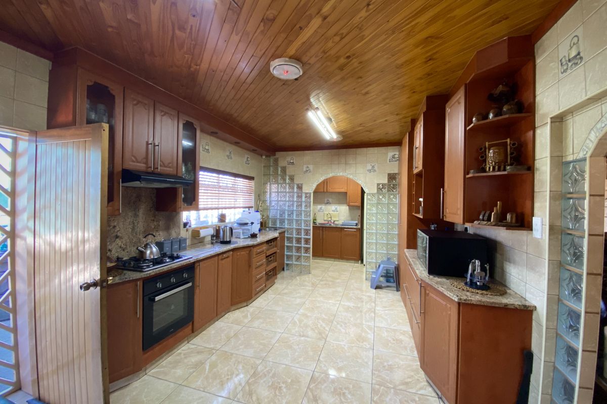 Spacious kitchen featuring extensive wooden cabinetry, granite countertops, built-in oven, gas hob, and a distinctive wooden tongue and groove ceiling.